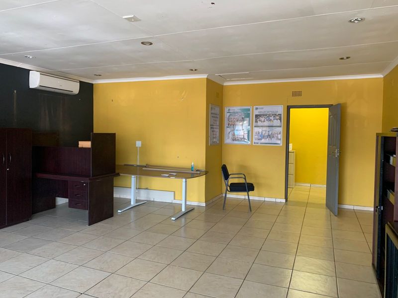 A functional office space featuring ceramic tiled flooring, recessed lighting, and a wall-mounted air conditioning unit, providing a practical workspace environment.