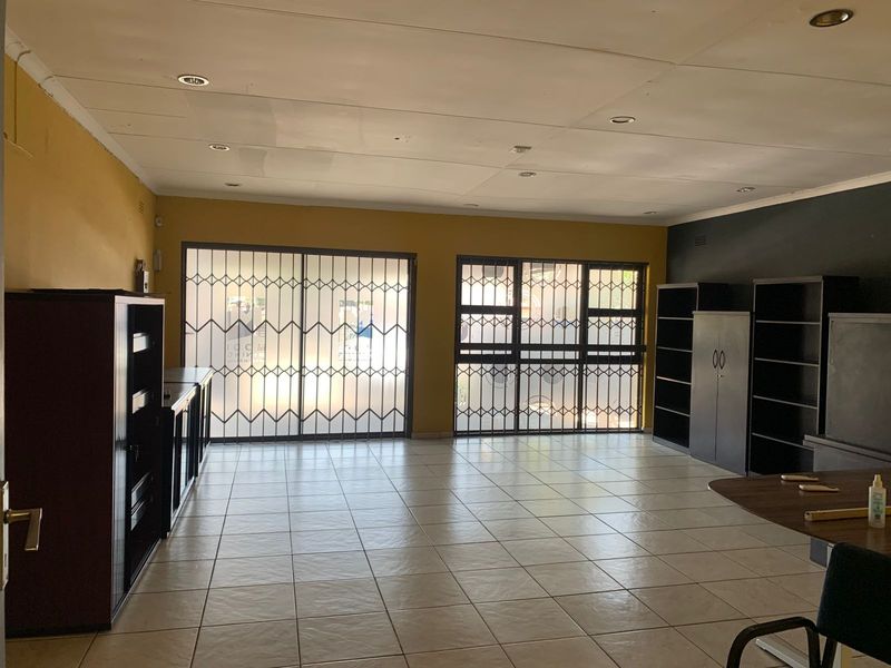 Spacious office area featuring tiled flooring, recessed lighting, and secure sliding glass doors with metal security gates.