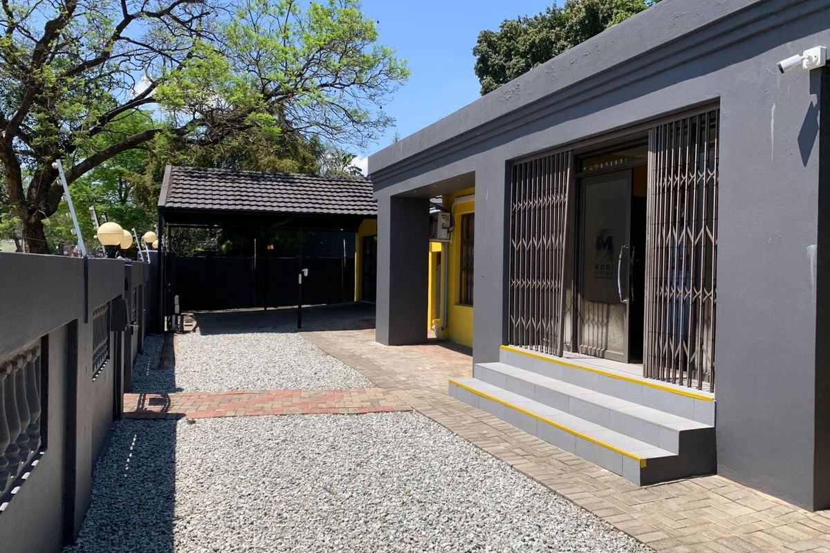 Front exterior view of the office property featuring a paved entrance, security gate, gravel driveway, and a covered carport area.