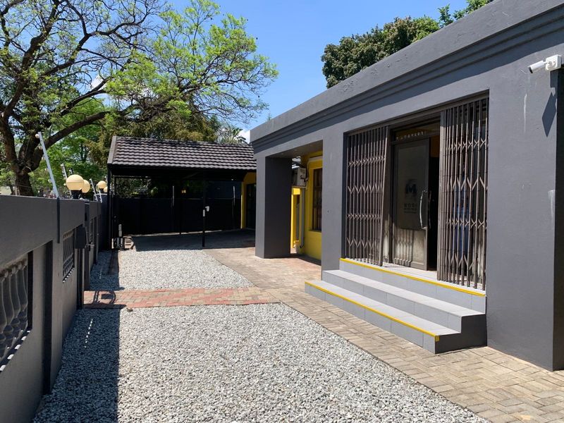 Front exterior view of the office property featuring a paved entrance, security gate, gravel driveway, and a covered carport area.