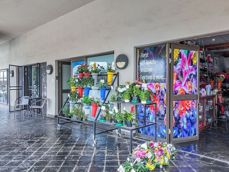 A commercial storefront featuring a covered walkway, stone tile flooring, and glass entrance doors, currently operating as a florist shop.