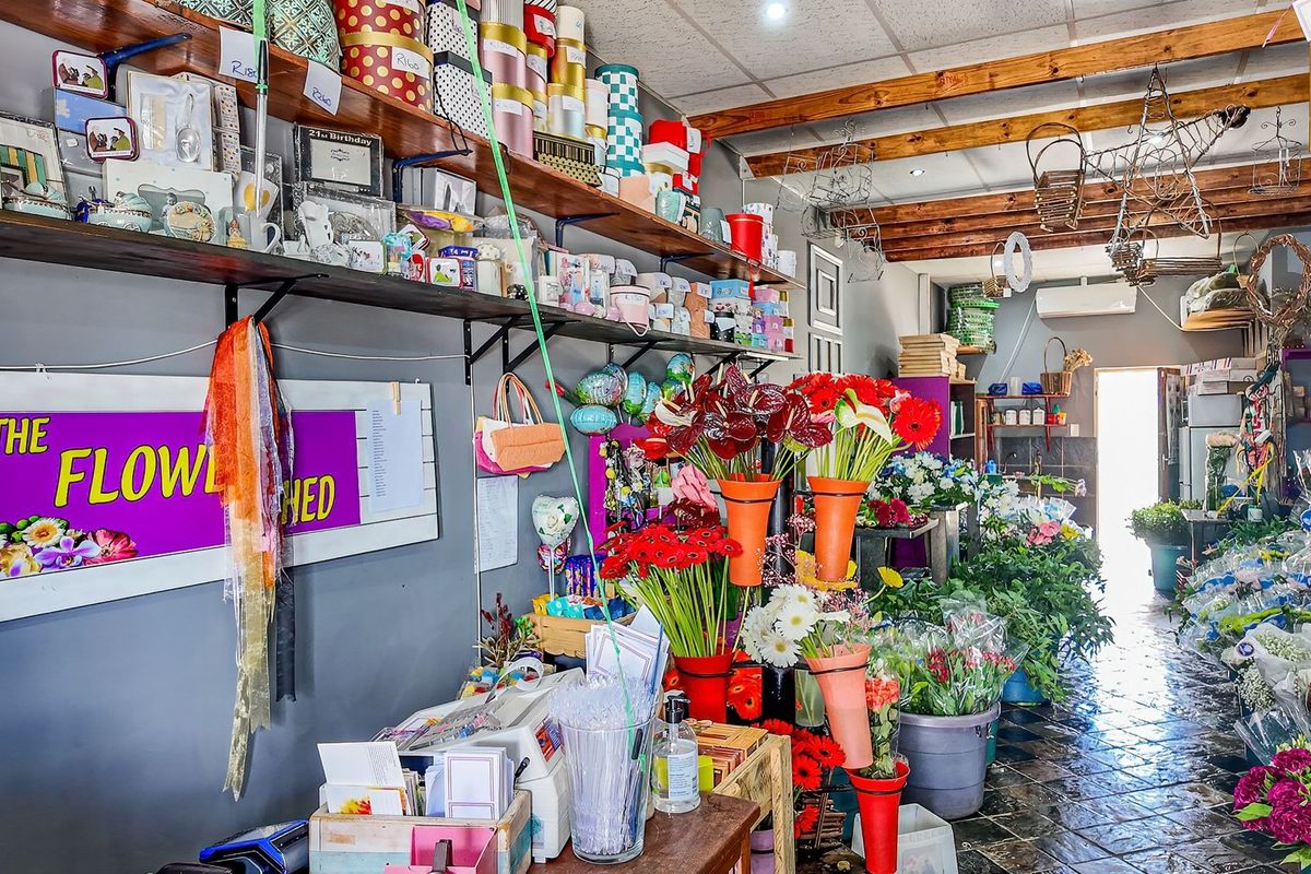 A commercial retail space featuring exposed timber ceiling beams, wall-mounted shelving, and durable tiled flooring, currently utilized as a floral shop.
