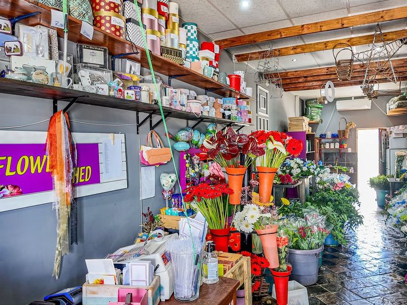 A commercial retail space featuring exposed timber ceiling beams, wall-mounted shelving, and durable tiled flooring, currently utilized as a floral shop.