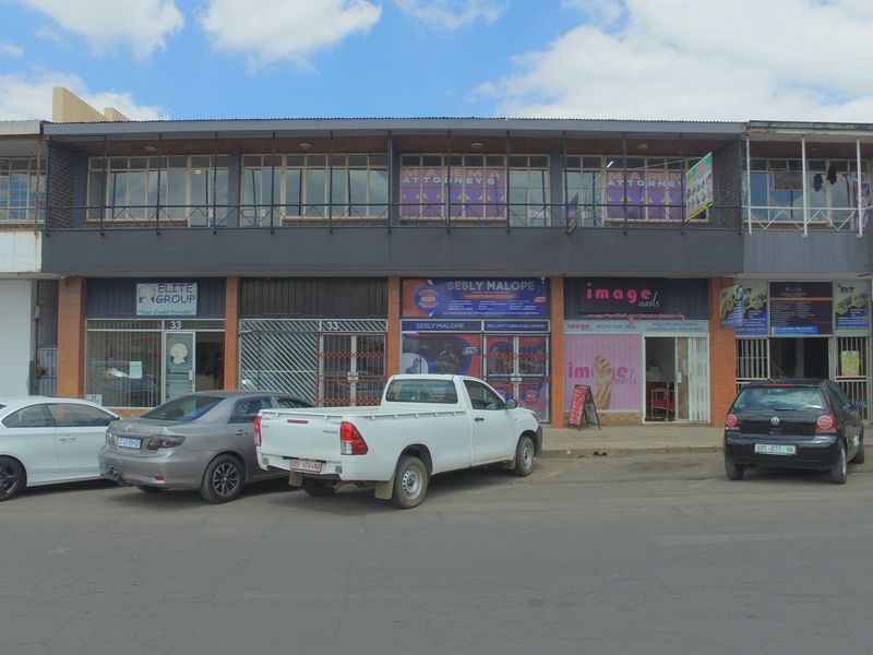 Front elevation of a multi-tenant retail building featuring ground-floor storefronts with security gates and upper-level office windows.