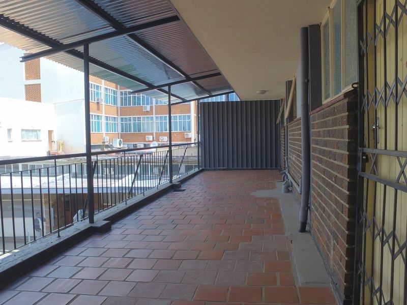 A covered outdoor balcony featuring tiled flooring, a corrugated metal roof, and metal security gate, providing an open-air space for the retail property.