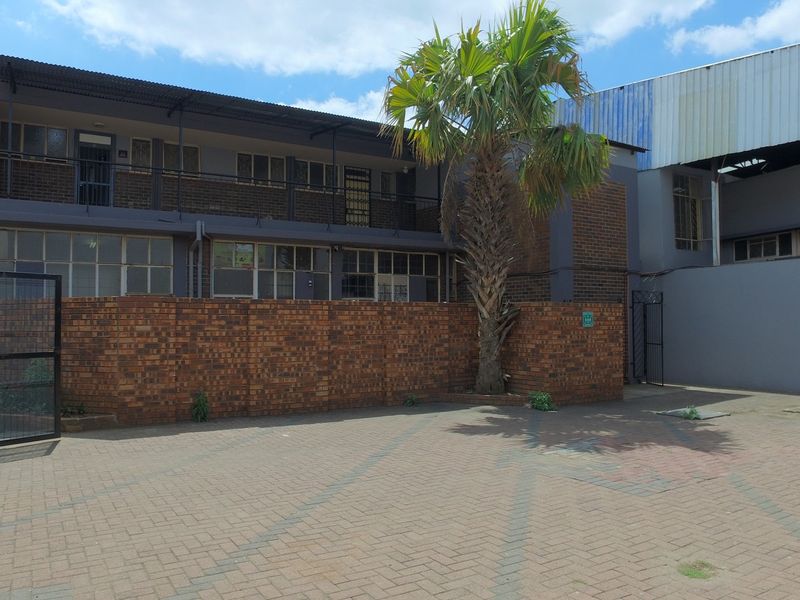 Rear exterior view of a multi-story commercial building featuring a paved courtyard, brick boundary wall, and metal security fencing.