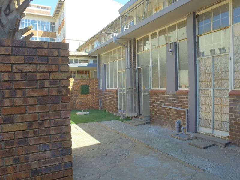Rear exterior courtyard featuring face brick walls, paved flooring, artificial grass, and multiple steel-framed access points to the building interior.
