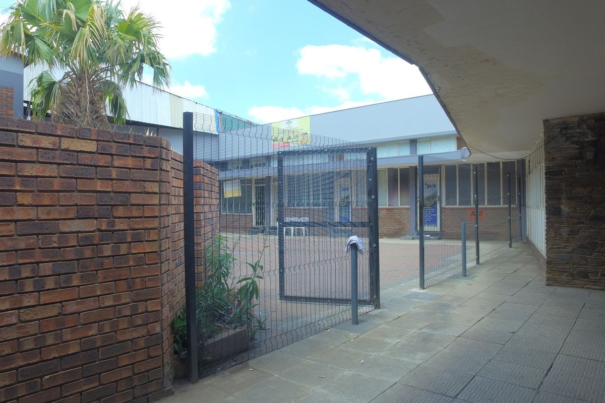 A paved rear courtyard area featuring brick boundary walls, mesh security fencing, and a covered walkway with visible signs of exterior wear.