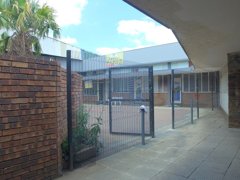 A paved rear courtyard area featuring brick boundary walls, mesh security fencing, and a covered walkway with visible signs of exterior wear.