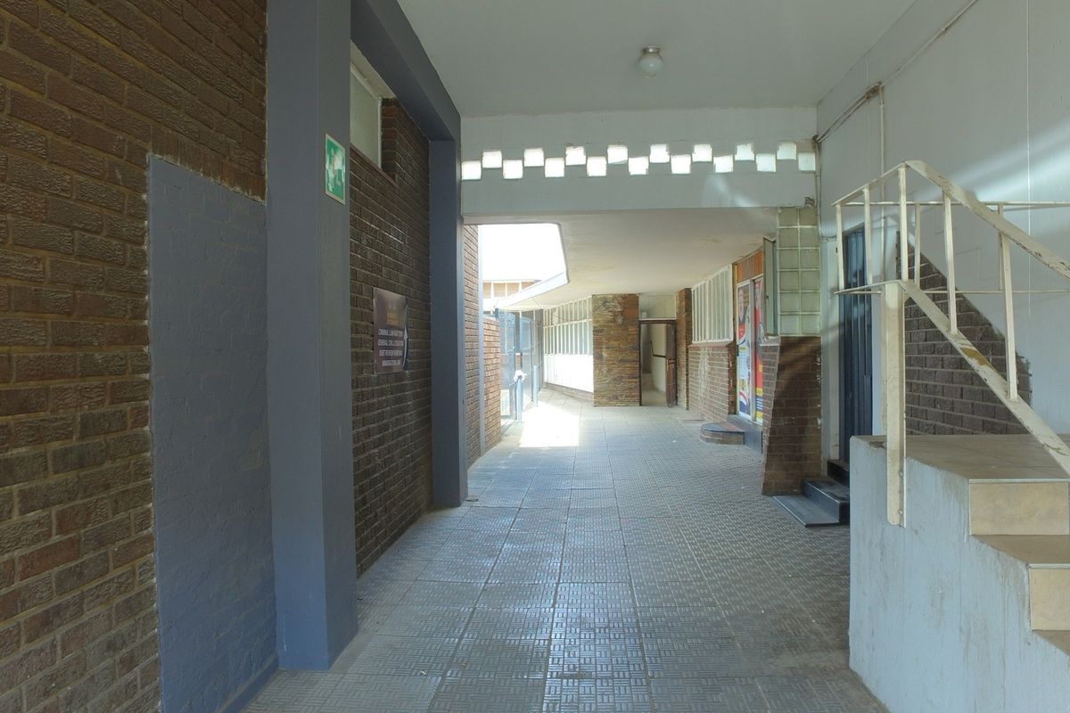 A covered outdoor walkway or corridor featuring brick walls, tiled flooring, and a metal staircase leading to upper levels of the retail property.