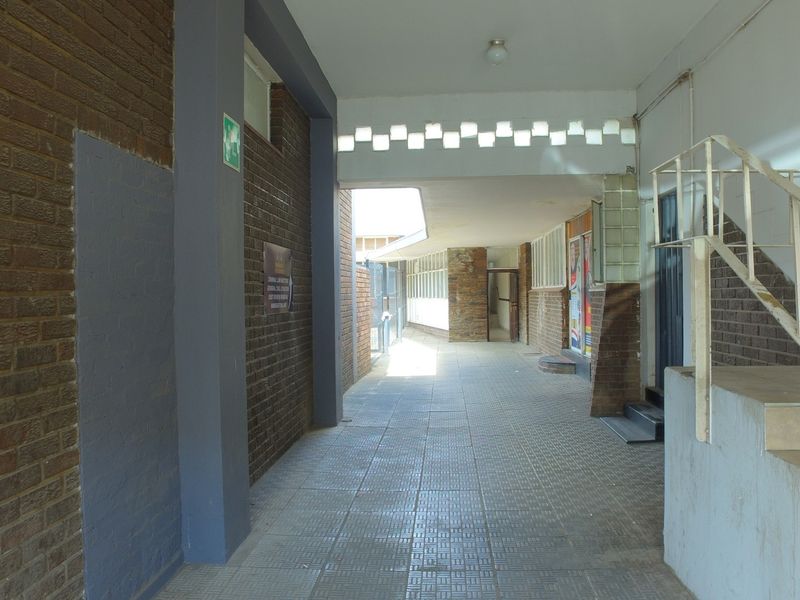 A covered outdoor walkway or corridor featuring brick walls, tiled flooring, and a metal staircase leading to upper levels of the retail property.