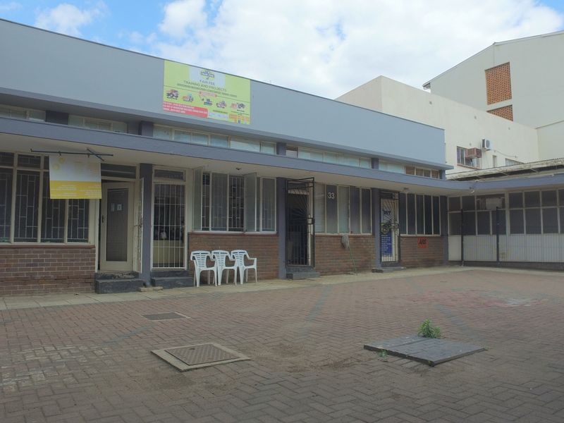 Rear exterior view of a commercial retail property featuring a paved courtyard, brick facade, and multiple secure access points.