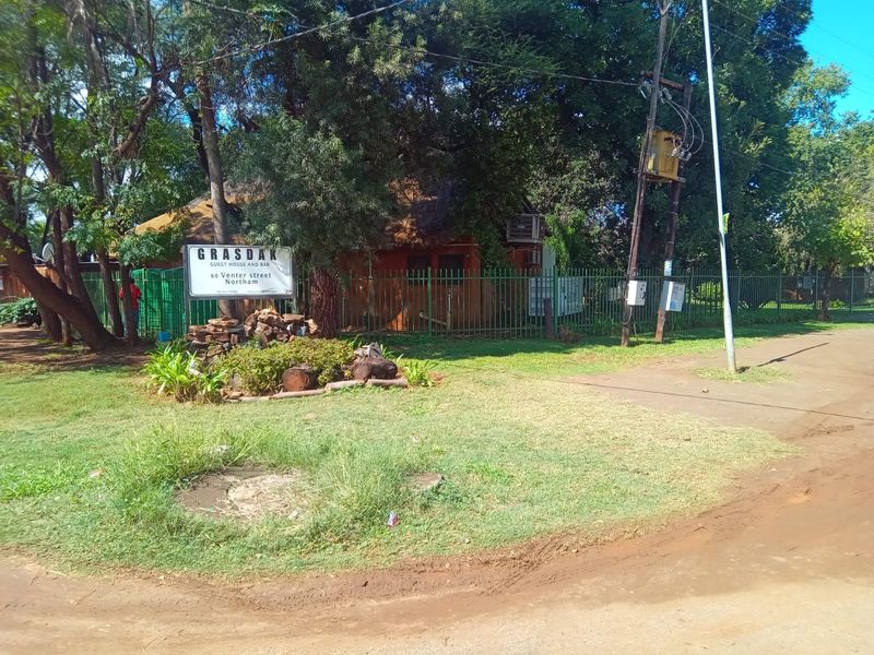 Street view of the guest house property entrance featuring perimeter fencing, signage, and established garden landscaping.