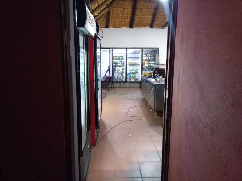 A rustic bar area featuring a traditional thatch roof, tiled flooring, and commercial refrigeration units, currently used as a service space.
