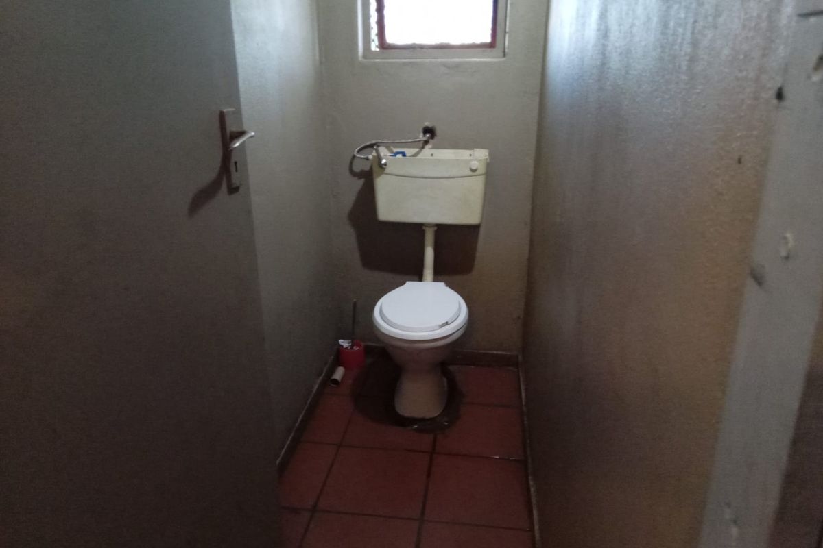 A small, functional bathroom featuring a standard toilet with a high-level cistern and tiled flooring, requiring cosmetic updates to improve its overall condition.
