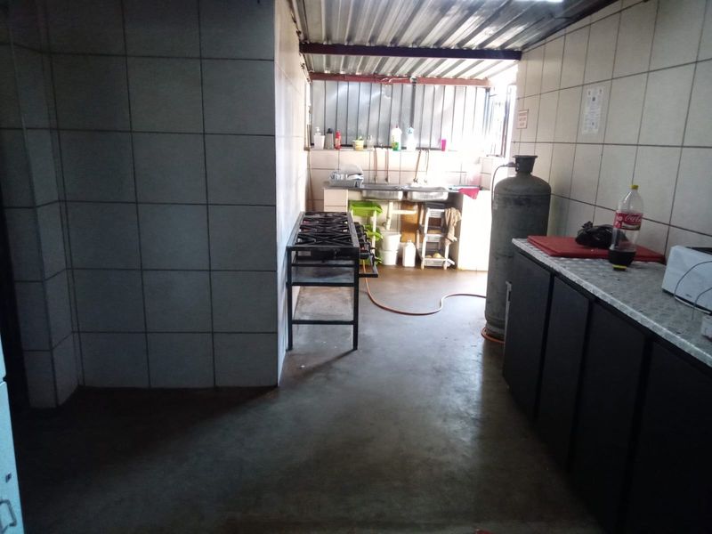 A functional kitchen area featuring tiled walls, a gas stove, and a stainless steel sink, with an industrial-style corrugated metal roof.
