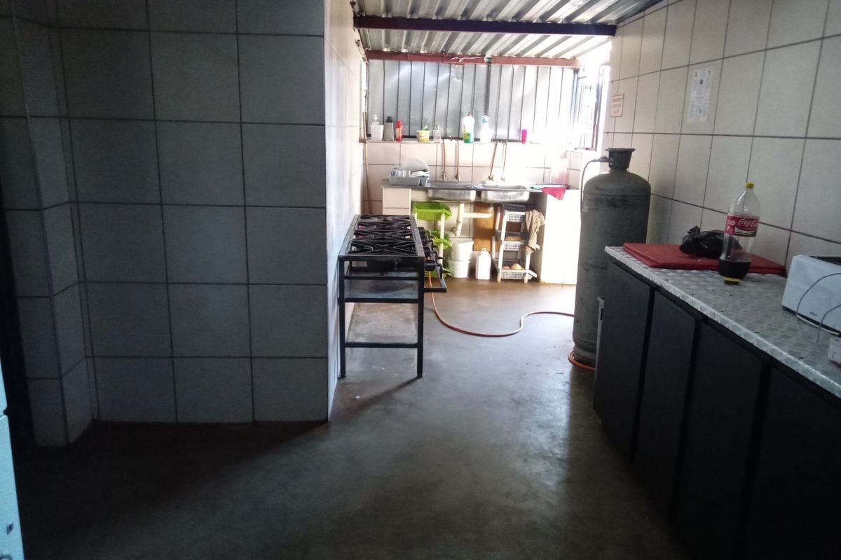 A functional kitchen area featuring tiled walls, a gas stove, and a stainless steel sink, with an industrial-style corrugated metal roof.