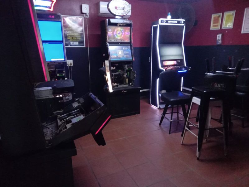 A dimly lit bar area featuring multiple gaming machines and tiled flooring, showing signs of wear and maintenance issues.
