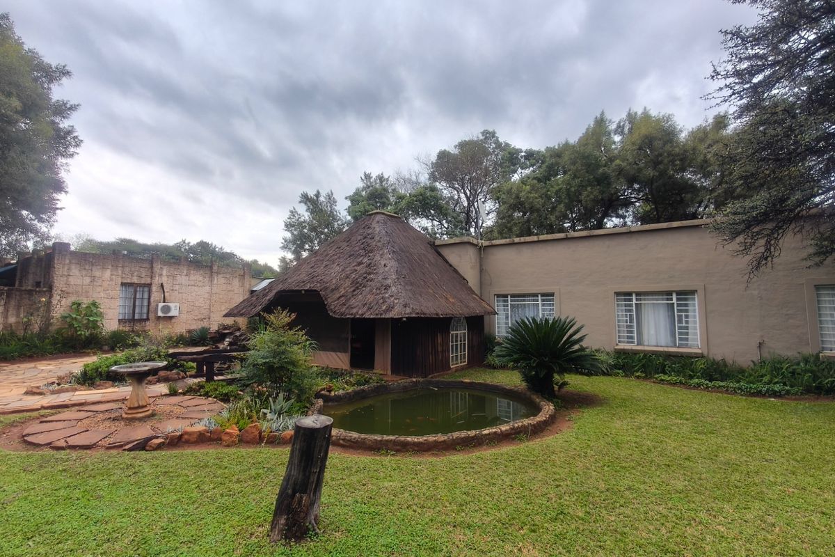 Rear garden view featuring a thatched roof structure, a small pond, and stone paved pathways set against the main dwelling.