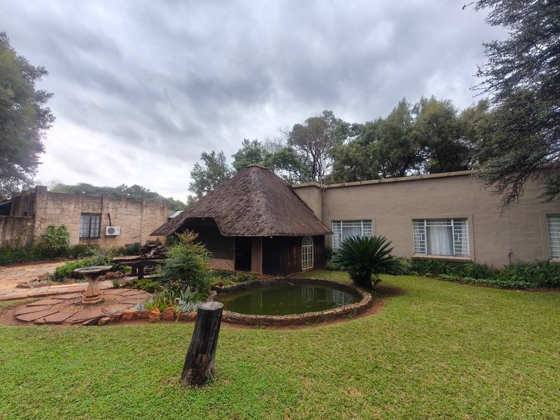 Rear garden view featuring a thatched roof structure, a small pond, and stone paved pathways set against the main dwelling.