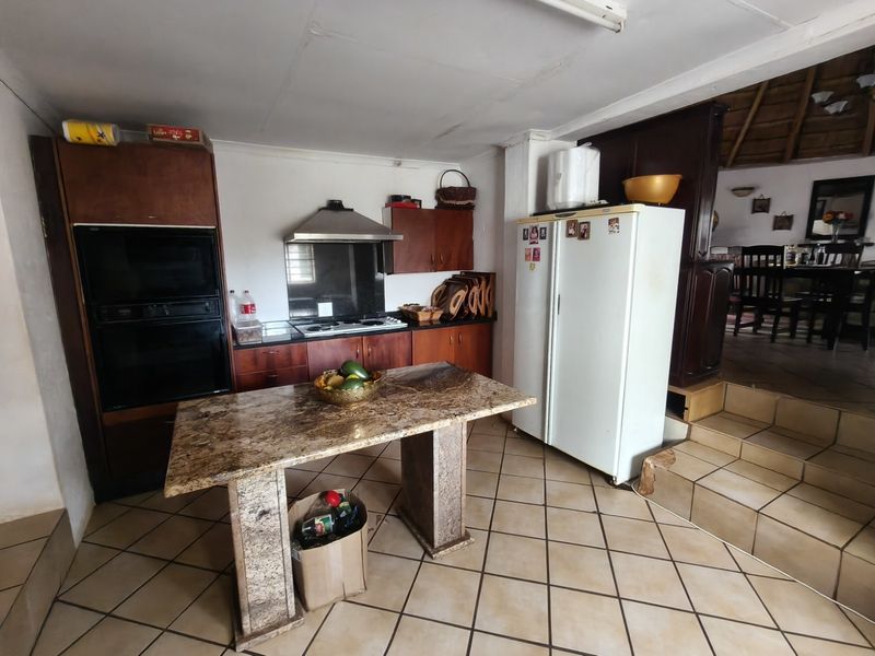 A functional kitchen featuring built-in cabinetry, a granite-topped island, and tiled flooring, with an open-plan layout leading to the dining area.