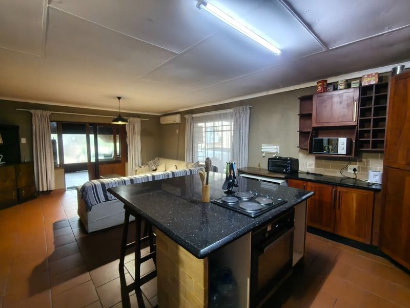 Open-plan living and kitchen area featuring a central island with built-in hob, granite countertops, wooden cabinetry, and direct access to an outdoor patio.