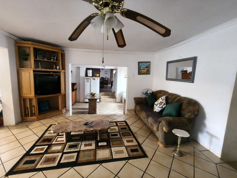 A living room featuring tiled flooring, a ceiling fan, and built-in wooden cabinetry, with an open-plan flow leading into the kitchen area.