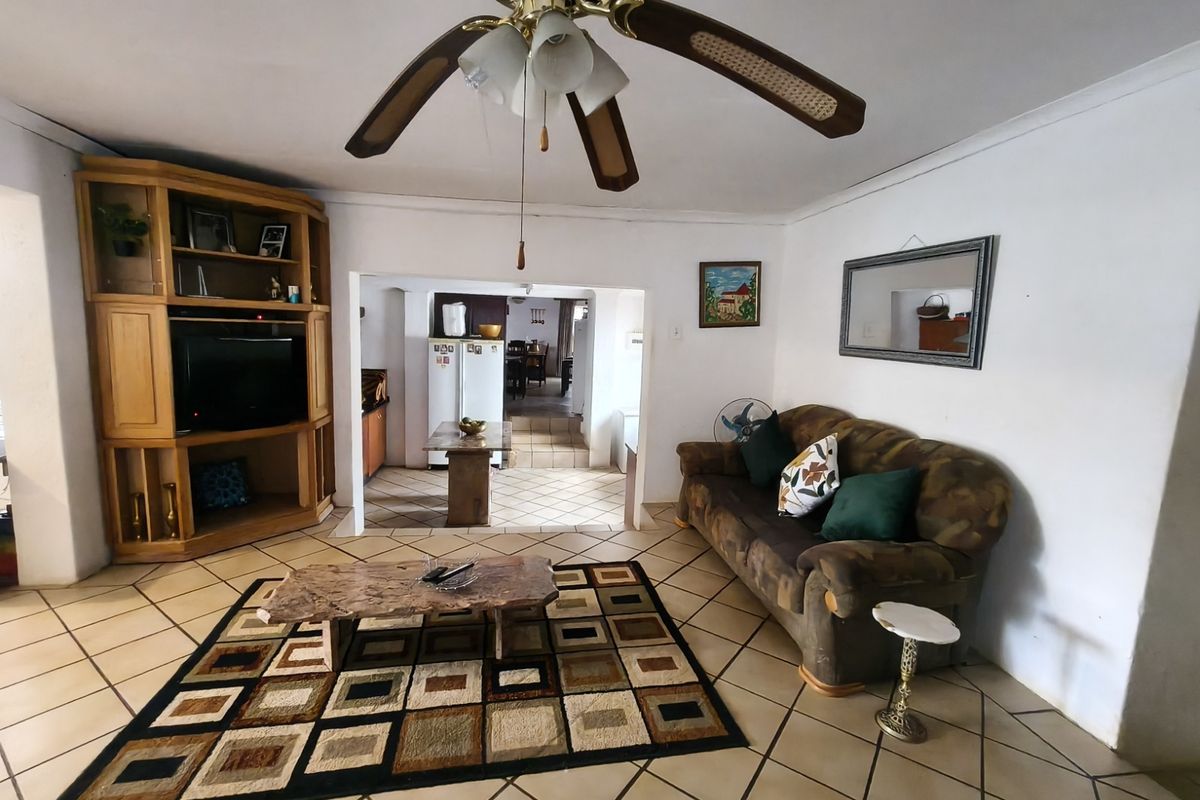 A living room featuring tiled flooring, a ceiling fan, and built-in wooden cabinetry, with an open-plan flow leading into the kitchen area.