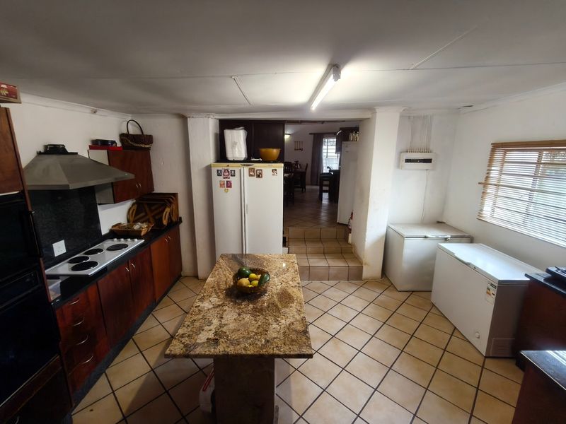 Spacious farm-style kitchen featuring dark wood cabinetry, a central granite island, tiled flooring, and direct access to the adjacent dining area.