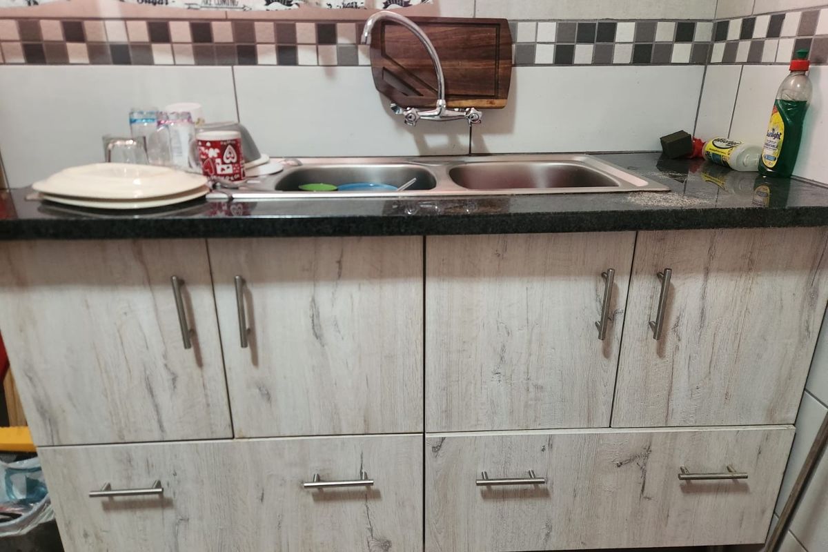 A functional kitchen area featuring a double bowl stainless steel sink, granite countertops, and light wood-grain laminate cabinetry with a tiled backsplash.