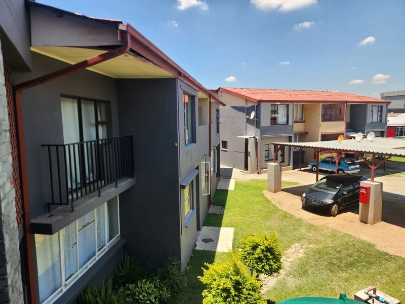 Exterior view of an apartment complex featuring multi-story units with balconies, a shared lawn area, and covered carport parking facilities.