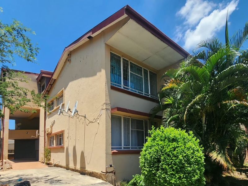 Exterior view of a multi-story apartment building featuring a concrete driveway, security bars on windows, and perimeter electric fencing.