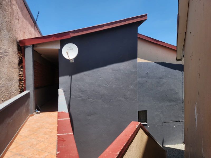 Exterior view of the apartment building showing a tiled walkway, dark grey painted walls, and a satellite dish installation.
