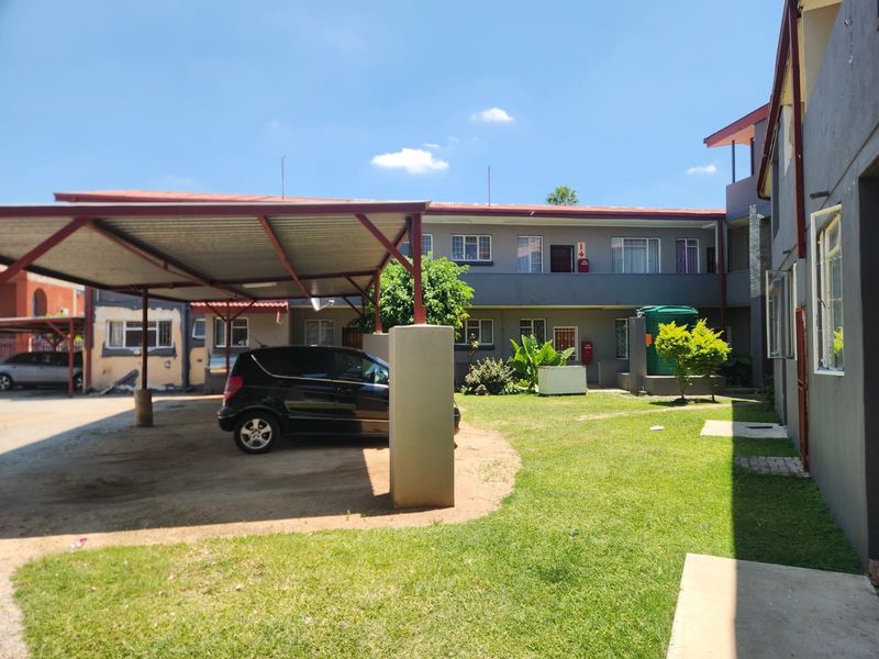 Exterior view of an apartment complex featuring a covered carport, communal lawn area, and water storage tank.