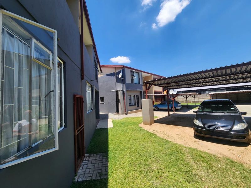 Exterior view of the apartment complex featuring a shared lawn area, covered carport parking, and paved walkways.