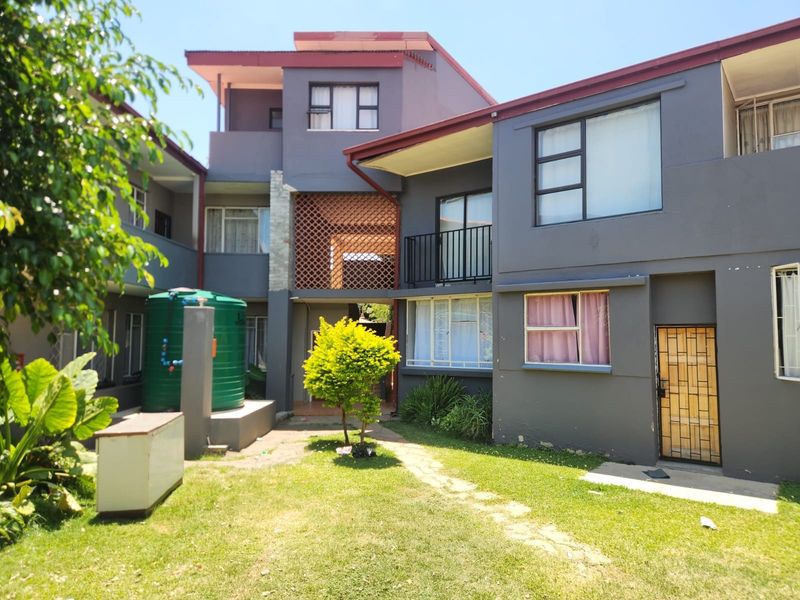 Rear view of the apartment complex featuring a communal garden area, water storage tank, and multi-level building facade with balcony access.