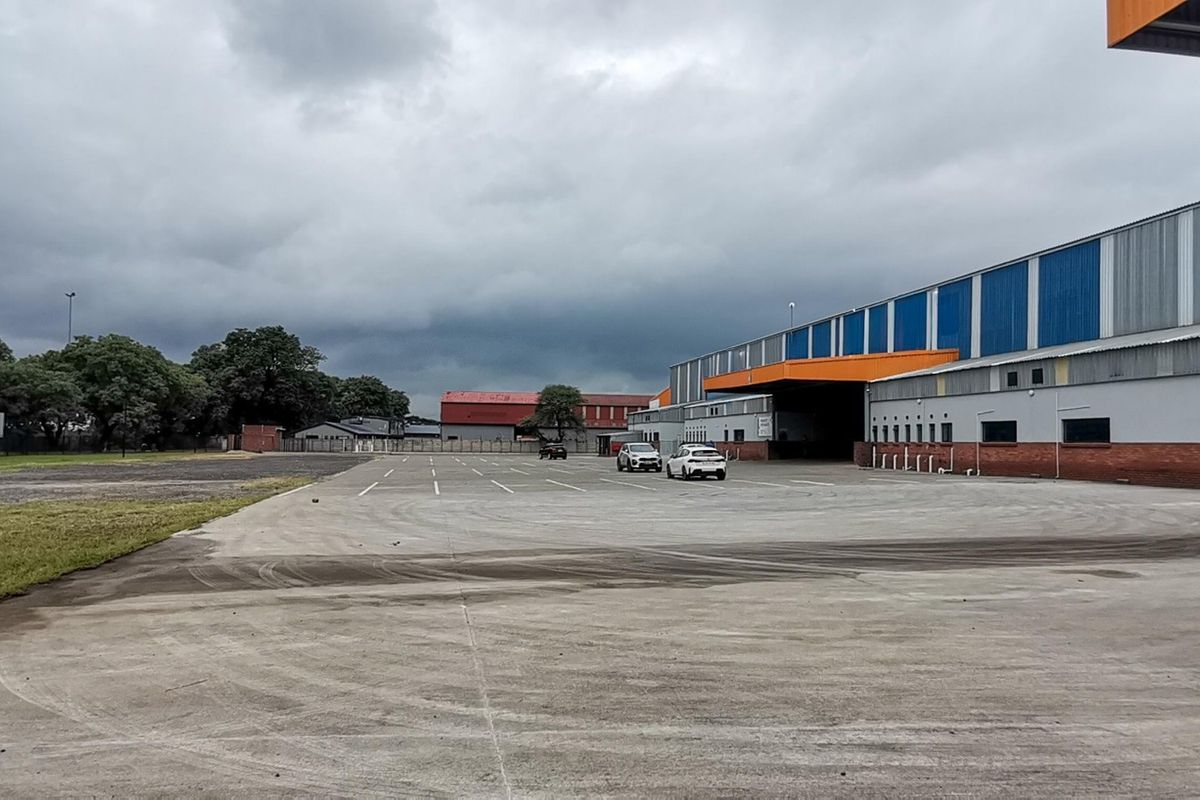 Wide view of an industrial property featuring a large concrete hardstand area, warehouse facade with metal cladding, and a covered loading bay.