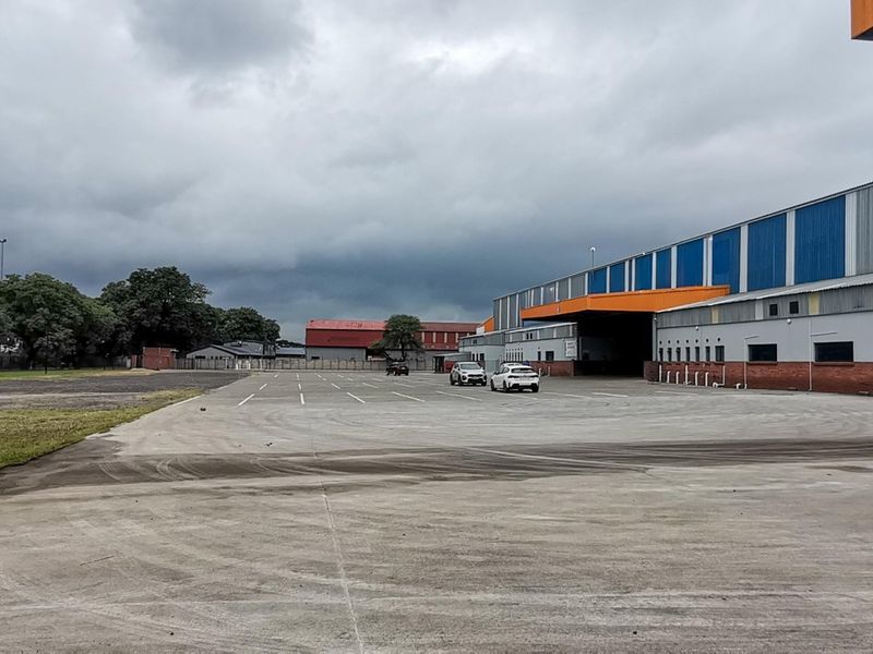 Wide view of an industrial property featuring a large concrete hardstand area, warehouse facade with metal cladding, and a covered loading bay.