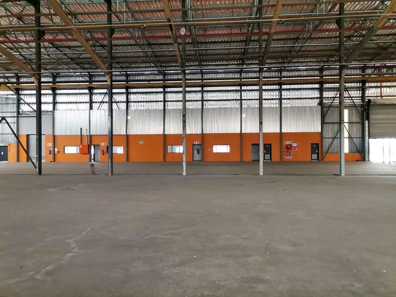 Spacious industrial warehouse unit featuring high ceilings with exposed steel trusses, concrete flooring, and functional wall-mounted fire safety equipment.