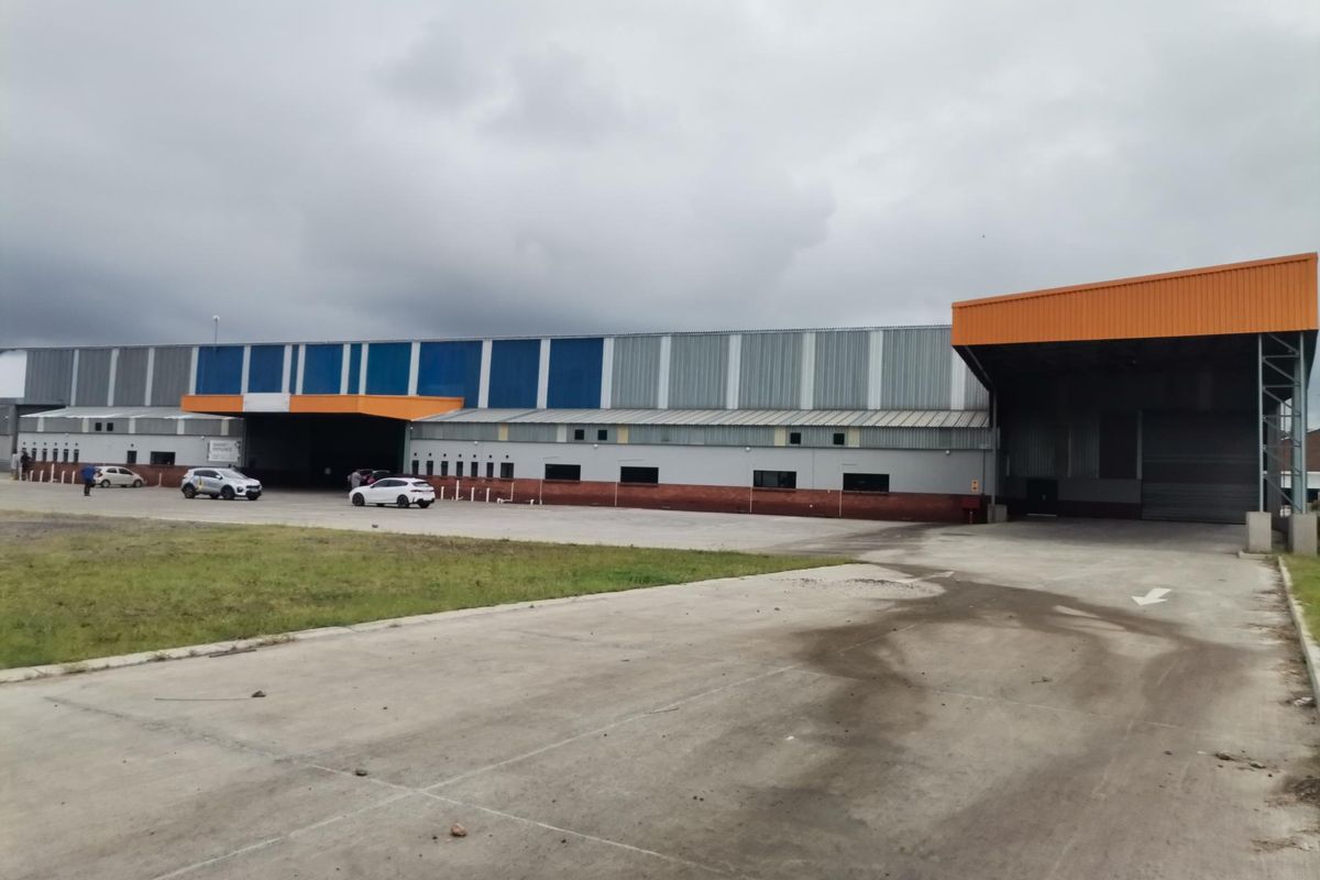 Large industrial warehouse facility featuring extensive metal cladding, multiple loading bays with roller shutter doors, and a spacious concrete yard area.