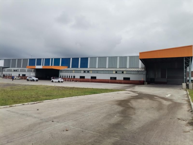 Large industrial warehouse facility featuring extensive metal cladding, multiple loading bays with roller shutter doors, and a spacious concrete yard area.