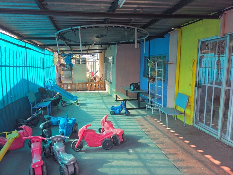 A covered outdoor patio area featuring concrete flooring, a corrugated metal roof, and access to the main building via a sliding glass door.