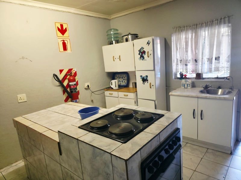 A functional kitchen featuring a tiled island with a built-in electric hob and oven, cabinetry, and a stainless steel sink.