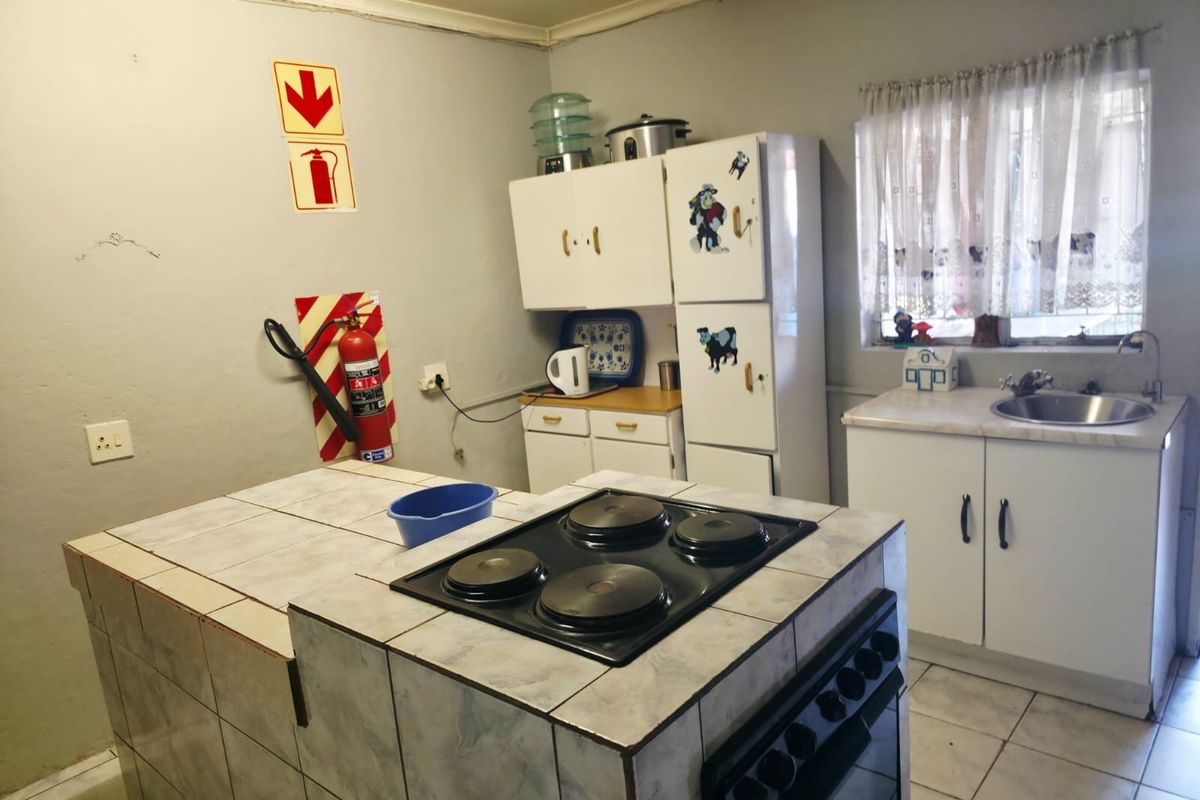 A functional kitchen featuring a tiled island with a built-in electric hob and oven, cabinetry, and a stainless steel sink.