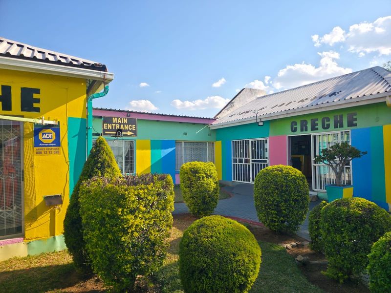 Front exterior view of a commercial creche facility featuring colorful painted walls, security gates, and a paved courtyard area.