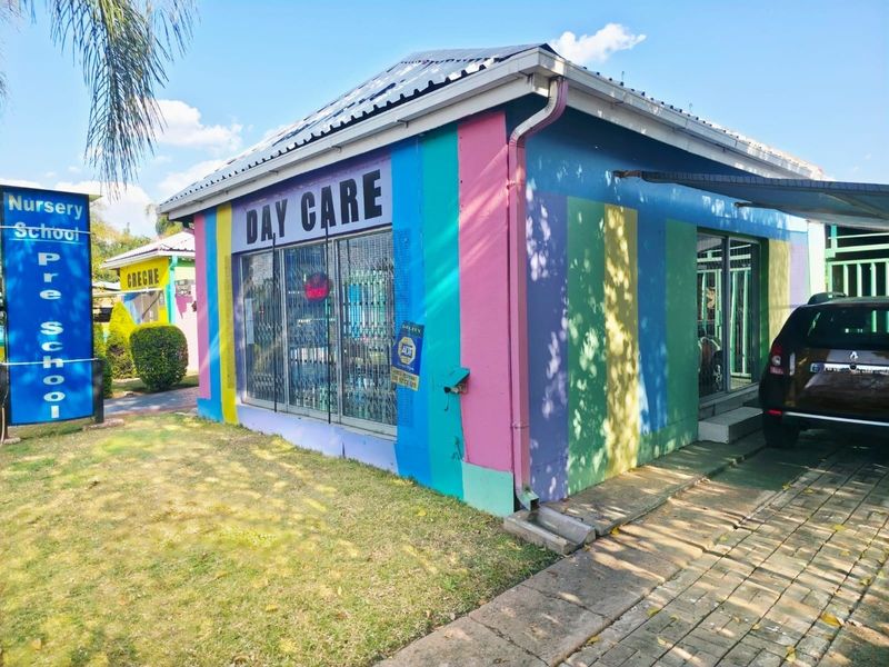 Exterior view of a nursery school facility featuring a colorful painted facade, metal security gates, and a paved driveway.