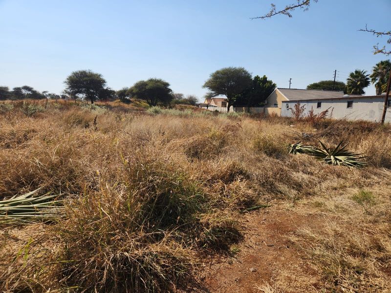 A view of a vacant commercial plot featuring natural vegetation and surrounding residential structures.
