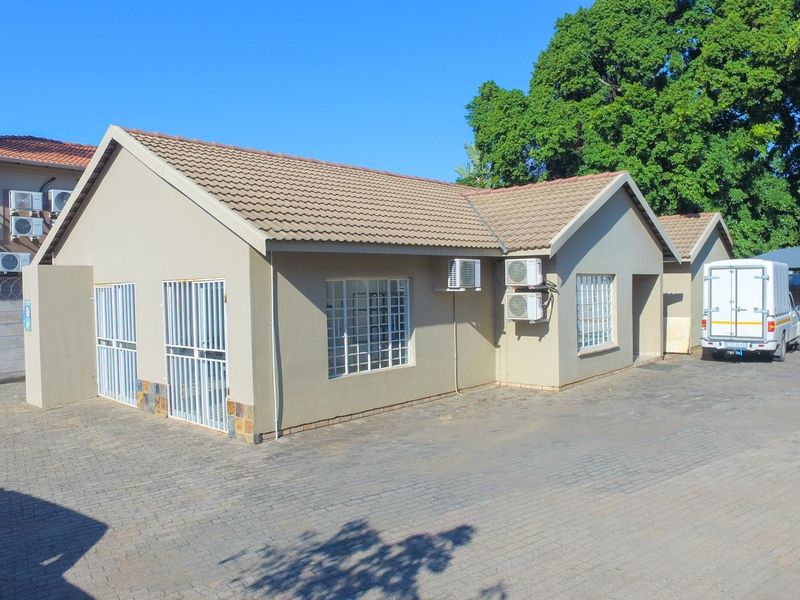 Exterior view of a single-story office building featuring a tiled roof, paved driveway, and multiple wall-mounted air conditioning units.