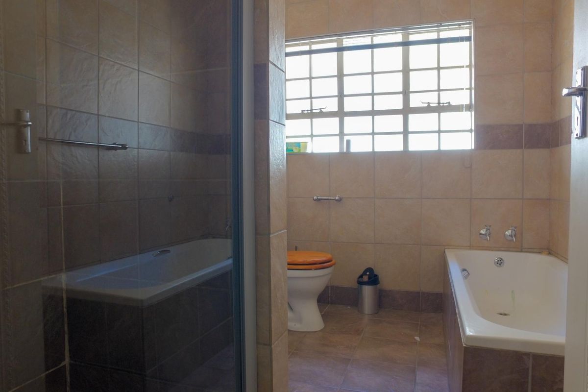 A functional bathroom featuring a bathtub, separate shower enclosure, and toilet, finished with neutral wall and floor tiles.