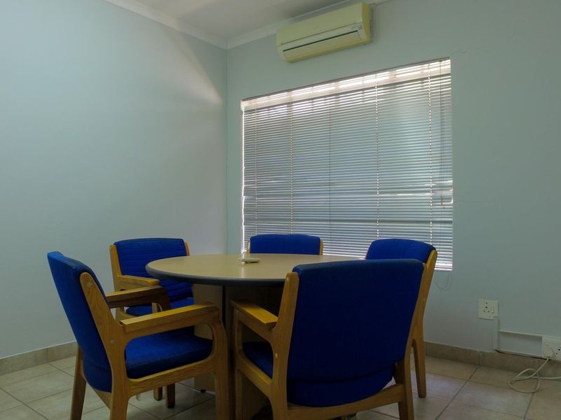 A functional office space featuring tiled flooring, a wall-mounted air conditioning unit, and window blinds, providing a clean and professional work environment.